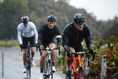 Dedicated male cyclists cycling on rainy road photo