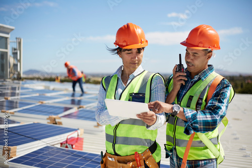 Engineers using walkie-talkie and digital tablet at solar power plant photo