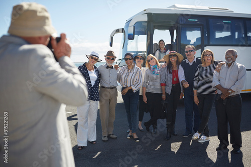 Active senior tourist friends posing for photograph outside tour bus