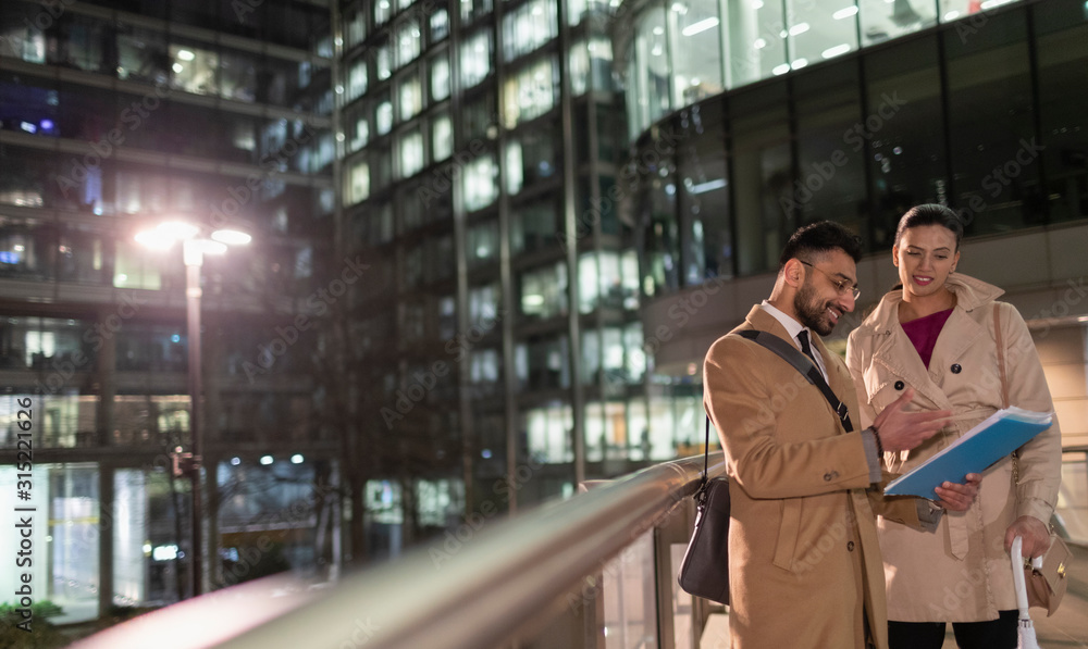 Business people discussing paperwork on urban pedestrian bridge at night Business people discussing paperwork on urban pedestrian bridge at night