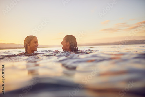 Young couple swimming in ocean at sunset photo