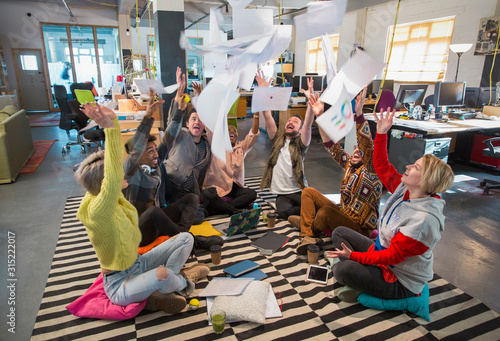 Playful, enthusiastic creative business team throwing paperwork overhead in open plan office