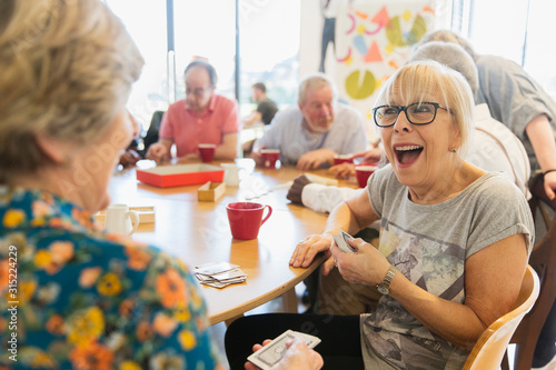 Happy senior woman playing cards with friend in community center photo