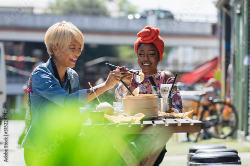 Happy young women friends enjoying dim sum lunch at sunny sidewalk cafe