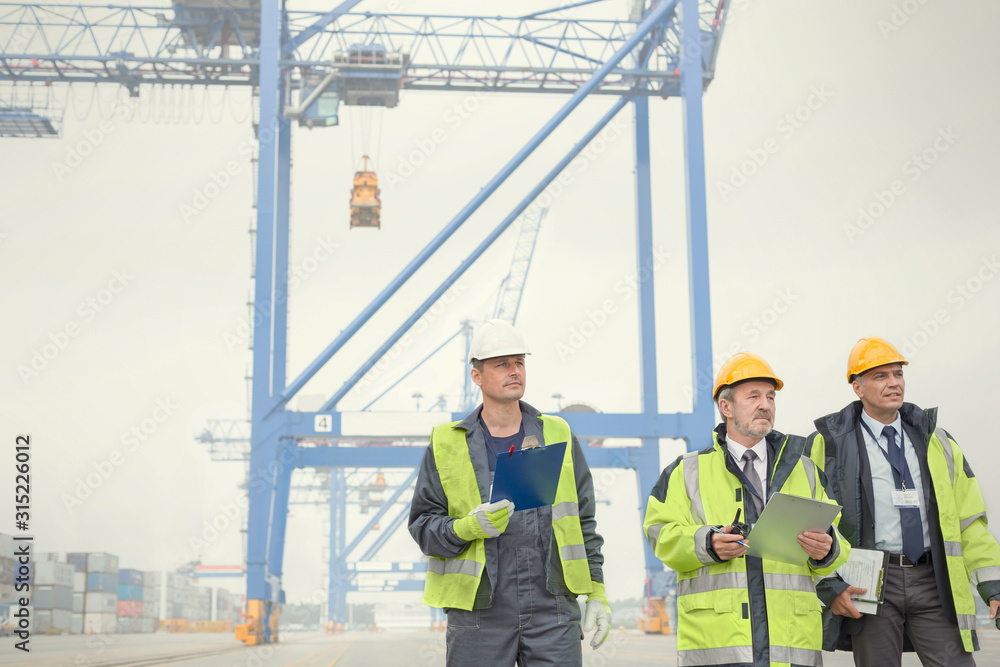 Dock workers and manager walking below crane at shipyard Dock workers and manager walking below crane at shipyard