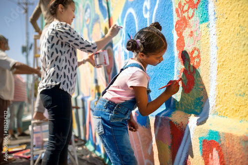 Girl volunteer painting vibrant mural on sunny wall