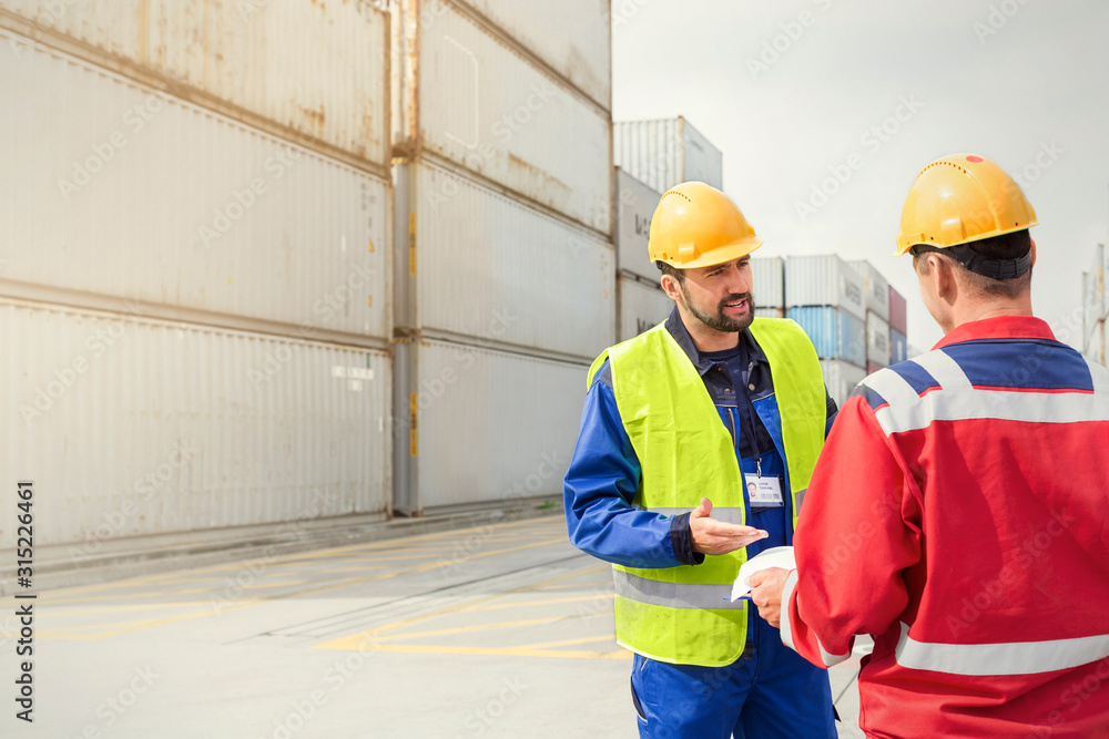 Dock workers talking near cargo containers at sunny shipyard Dock workers talking near cargo containers at sunny shipyard