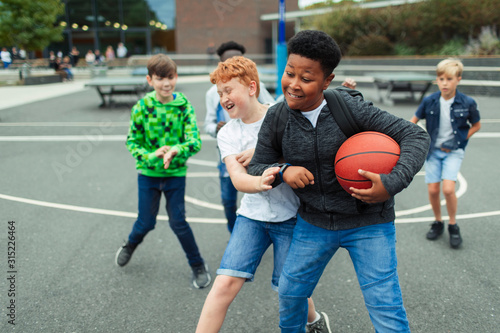 Tween boys playing basketball in schoolyard photo