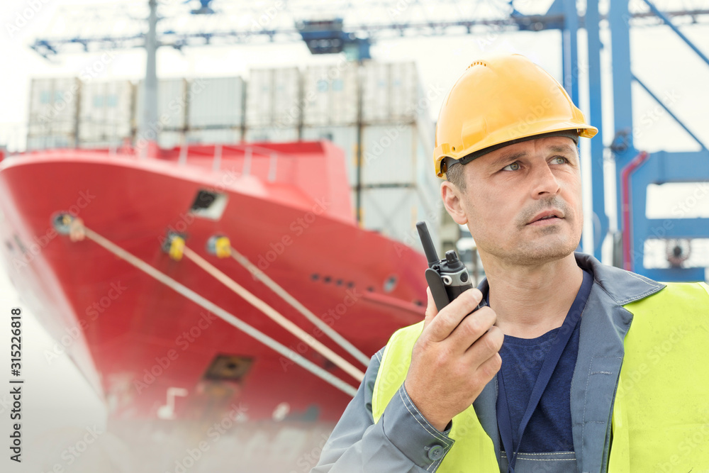 Dock worker using walkietalkie below container ship at shipyard Stock