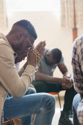 Serene man praying with rosary in prayer group