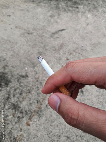 Cigarette pick by hand with concrete background.