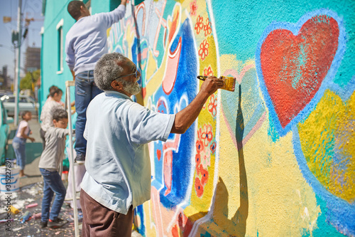 Senior man painting mural on sunny urban wall photo