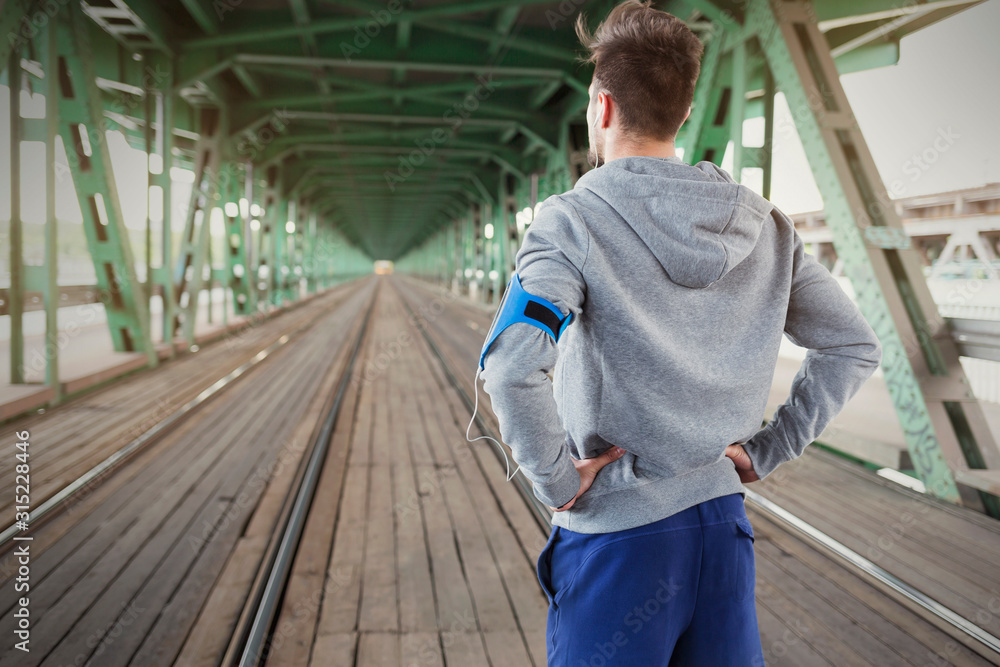 Young male runner standing on train tracks with hands on hips Young male runner standing on train tracks with hands on hips