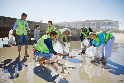 Volunteers cleaning up litter on sunny, wet sand beach photo
