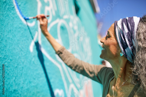 Senior woman painting mural on sunny wall photo