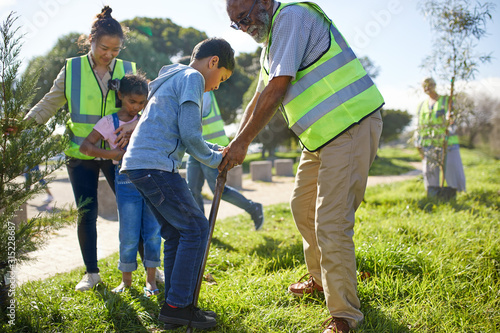 Multi-generation family volunteers planting trees in sunny park