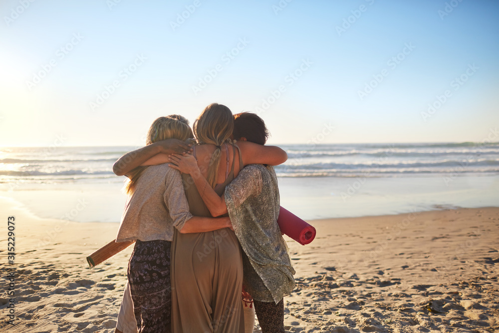Female friends with yoga mats hugging on sunny beach Female friends with yoga mats hugging on sunny beach