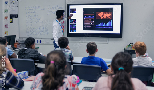 Male teacher leading lesson at touch screen television in classroom photo