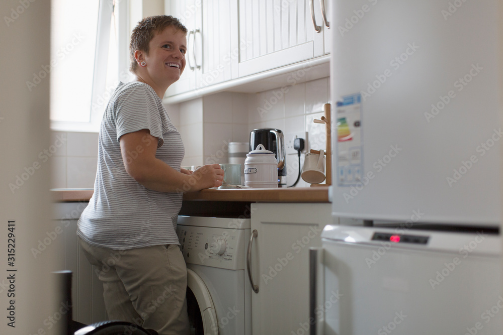 Smiling young woman preparing tea in apartment kitchen