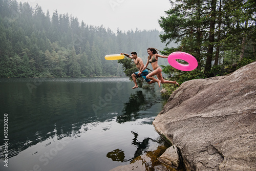 Playful young couple inflatable rings jumping into remote lake, Squamish, British Columbia, Canada