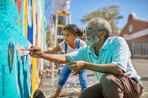 Grandfather granddaughter volunteers painting vibrant mural on sunny urban wall