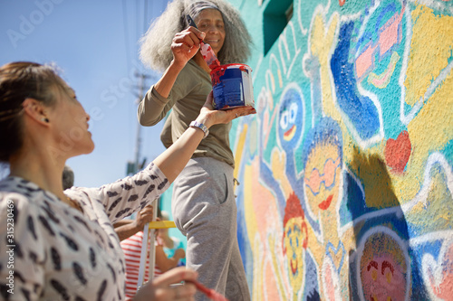 Female volunteers painting vibrant community mural on sunny urban wall photo