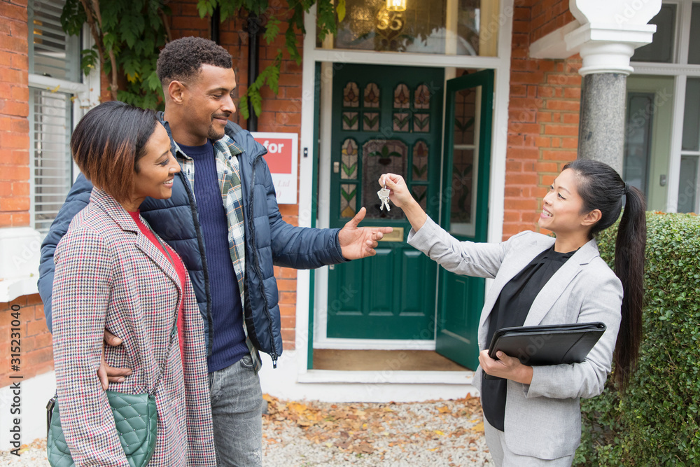 Real estate agent giving house keys to couple outside new house Stock ...