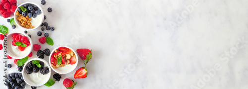 Healthy yogurt bowls with assorted berries and granola. Banner with corner border against a white marble background. Copy space.