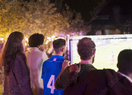 Friends watching soccer match on projection screen in backyard