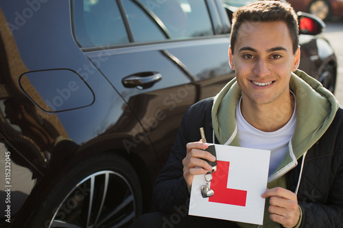 Portrait confident, happy young man holding learners permit by car photo