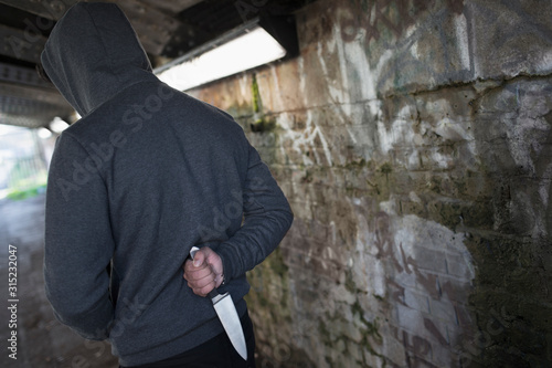 Dangerous man with knife behind back in urban tunnel