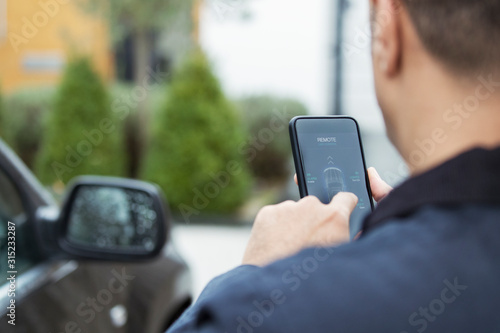 Man setting car alarm from smart phone in driveway photo