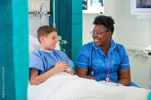 Female nurse talking with boy patient in hospital room photo