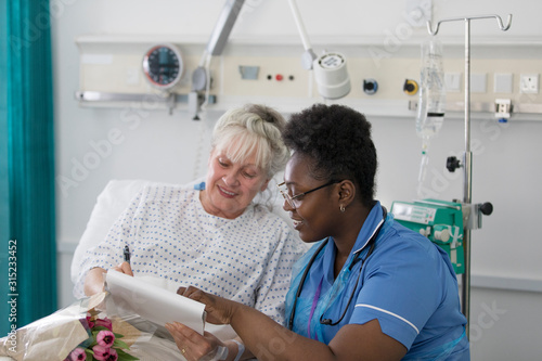 Female nurse discussing paperwork with senior patient in hospital room photo