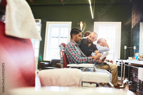 Male barber and customer with digital tablet talking in barbershop photo