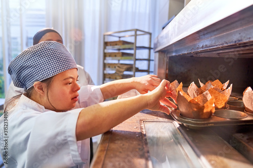 Young woman with Down Syndrome placing muffins in oven photo