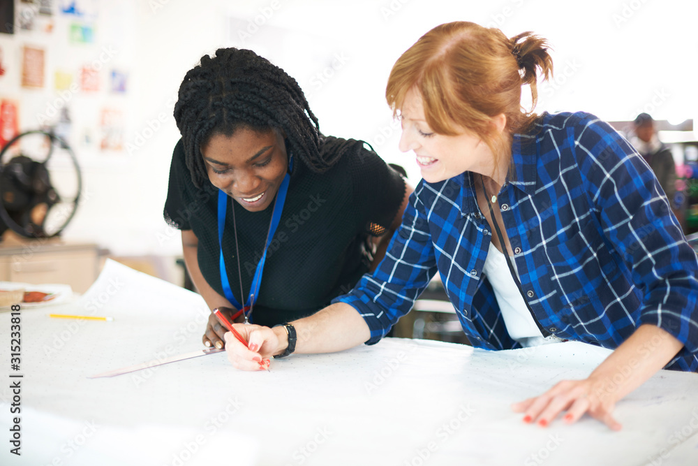 Female fashion designers drawing sewing pattern in studio Female fashion designers drawing sewing pattern in studio