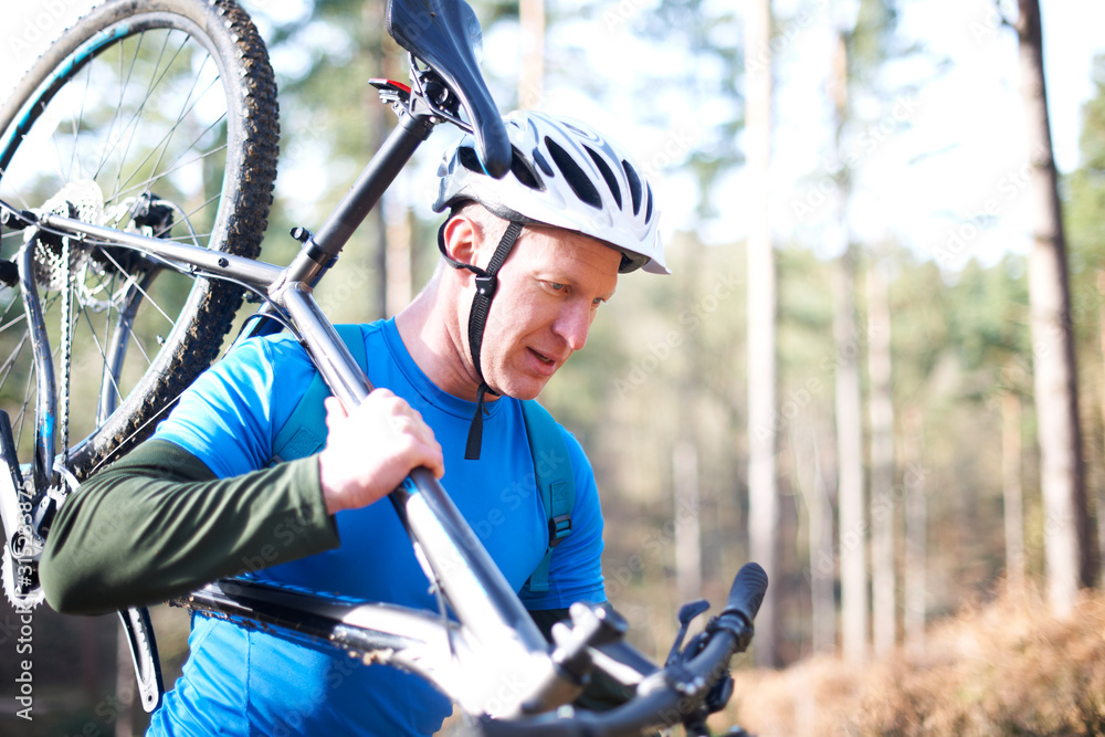 Male cyclist carrying bicycle in sunny woods Male cyclist carrying bicycle in sunny woods