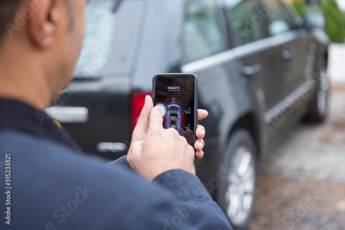 Man setting car alarm with smart phone in driveway photo