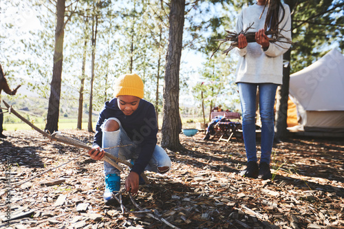 Boy picking up sticks for firewood at sunny campsite in woods photo