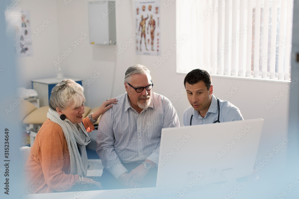 Doctor meeting with senior couple at computer in doctors office Doctor meeting with senior couple at computer in doctors office