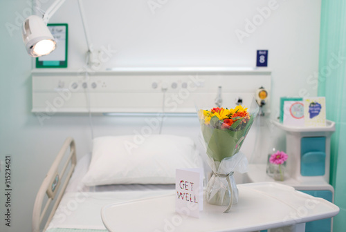 Flower bouquet and Get Well greeting card on tray in vacant hospital room photo