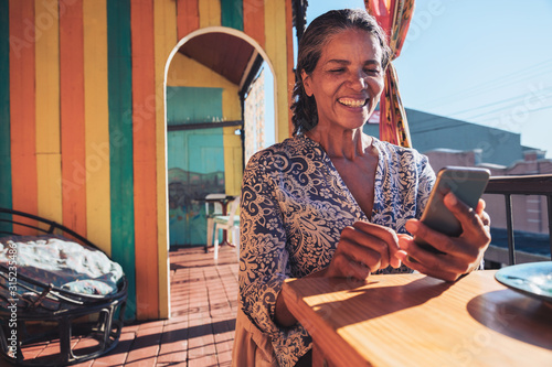 Smiling, happy woman using smart phone on sunny restaurant balcony photo