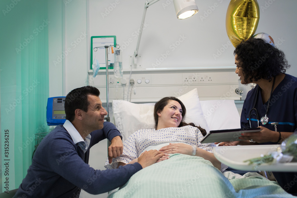Doctor with digital tablet making rounds, talking with couple in hospital room