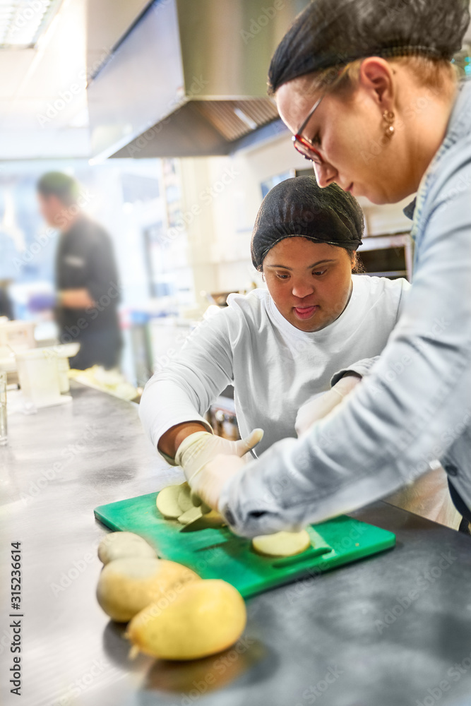 Chef and young woman with Down Syndrome cutting potatoes in kitchen Chef and young woman with Down Syndrome cutting potatoes in kitchen