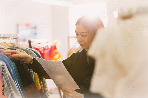 Fashion buyer reviewing paperwork at clothing racks photo