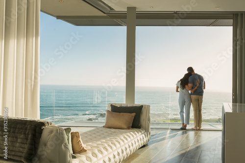 Affectionate couple hugging on sunny luxury balcony with ocean view photo
