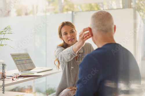 Female doctor helping male patient with hearing aid in doctor‚Äôs office