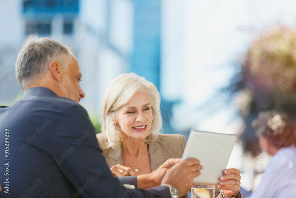 Businessman and businesswoman using digital tablet at urban sidewalk cafe Businessman and businesswoman using digital tablet at urban sidewalk cafe