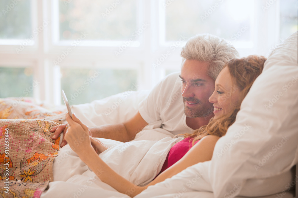 Couple relaxing laying in bed using digital tablet Couple relaxing laying in bed using digital tablet
